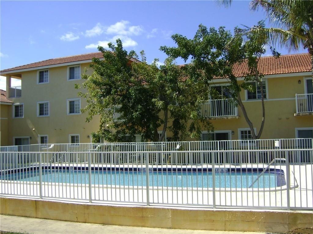 A swimming pool sits in front of a multi-story apartment building with a tiled roof — NORTH MIAMI BEACH, FL