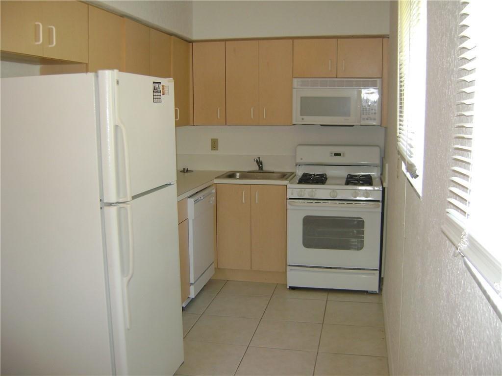 A kitchen features light wood cabinets, white appliances, and light-colored tile flooring — NORTH MIAMI BEACH, FL