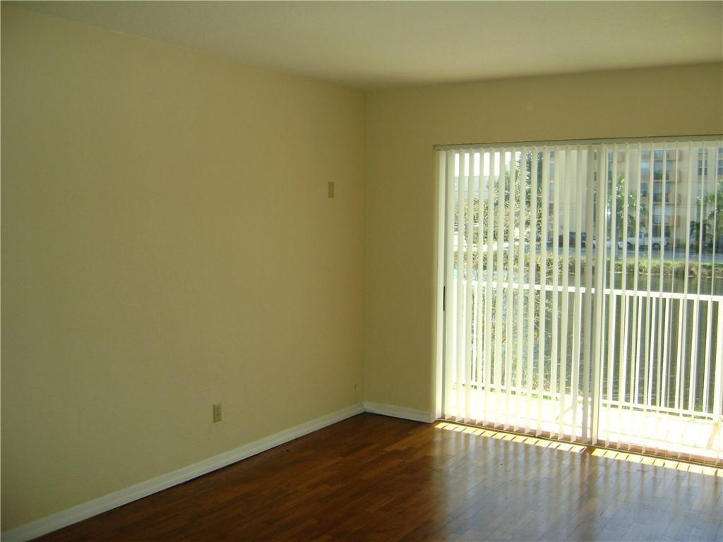 An empty room with hardwood floors, beige walls, and sliding glass doors leading to a balcony — NORTH MIAMI BEACH, FL