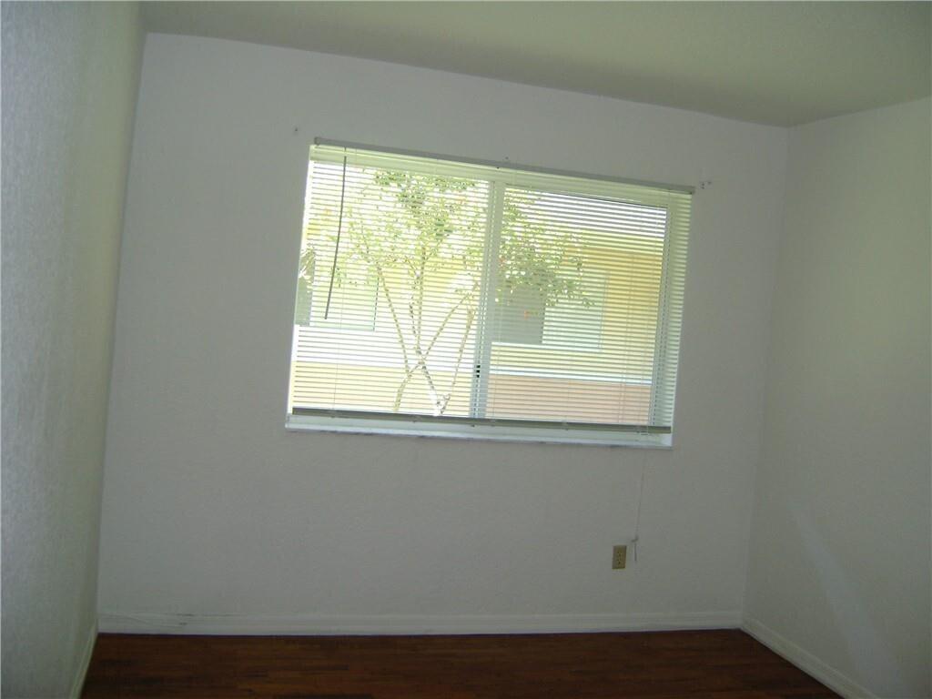 An empty room features white walls, dark wood-look flooring, and a window with horizontal blinds — NORTH MIAMI BEACH, FL