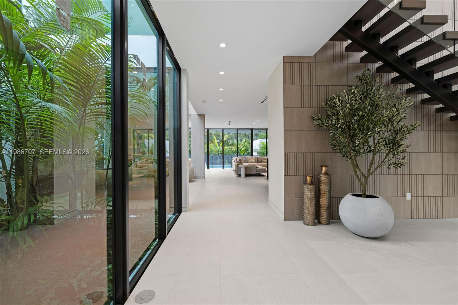 A modern hallway features a glass-walled courtyard, a floating staircase, and textured wood paneling — 4534 Sheridan Ave, Miami Beach FL 33140, MIAMI BEACH, FL