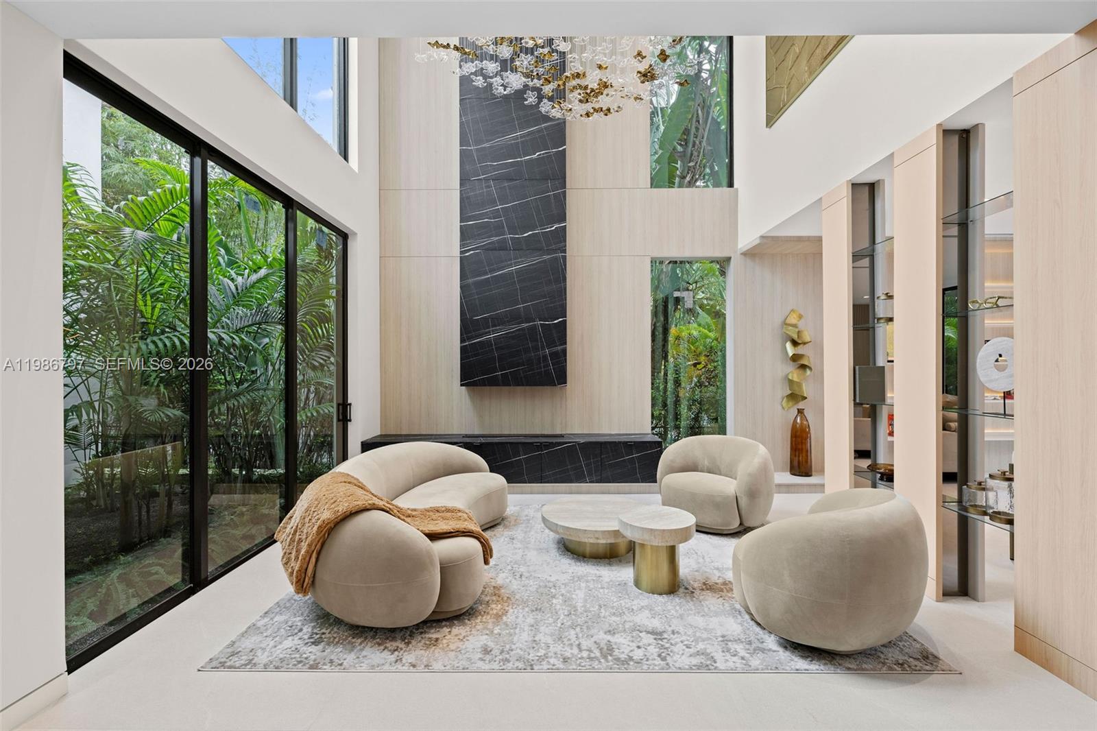 A modern living room features a double-height ceiling, marble fireplace, and floor-to-ceiling glass walls — 4534 Sheridan Ave, Miami Beach FL 33140, MIAMI BEACH, FL