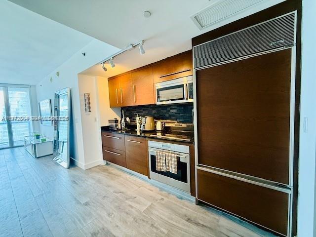 A modern kitchen features wood cabinetry, stainless steel appliances, and light-colored wood flooring — 475 Brickell Ave # 4910, Miami FL 33131, MIAMI, FL