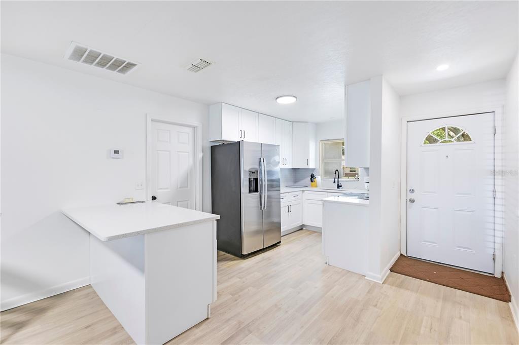 A kitchen features white cabinets, stainless steel appliances, a peninsula, and light-colored wood flooring — 1725 CALIFORNIA AVENUE, ST CLOUD, FL