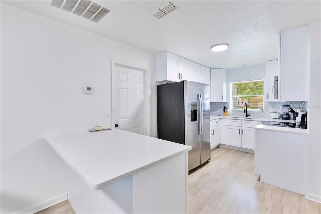 A modern kitchen features white cabinets, stainless steel appliances, and a white quartz breakfast bar — 1725 CALIFORNIA AVENUE, ST CLOUD, FL