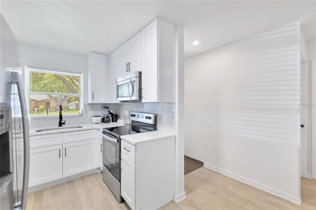 A bright kitchen features white cabinets, stainless steel appliances, and light wood-look flooring — 1725 CALIFORNIA AVENUE, ST CLOUD, FL