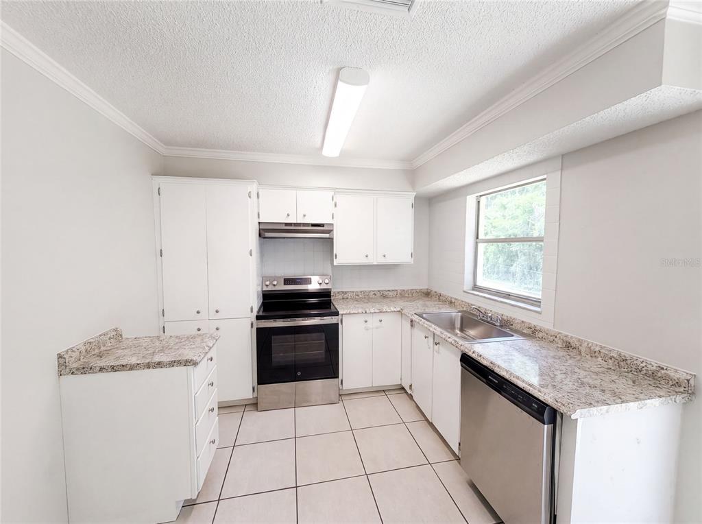 A kitchen features white cabinets, granite-look countertops, stainless steel appliances, and light-colored floor tiles — 3730 DEDRICK COURT, NEW PORT RICHEY, FL