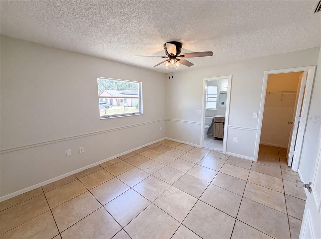 A bedroom with beige tile flooring, chair rail molding, a ceiling fan, and an attached bathroom — 3730 DEDRICK COURT, NEW PORT RICHEY, FL