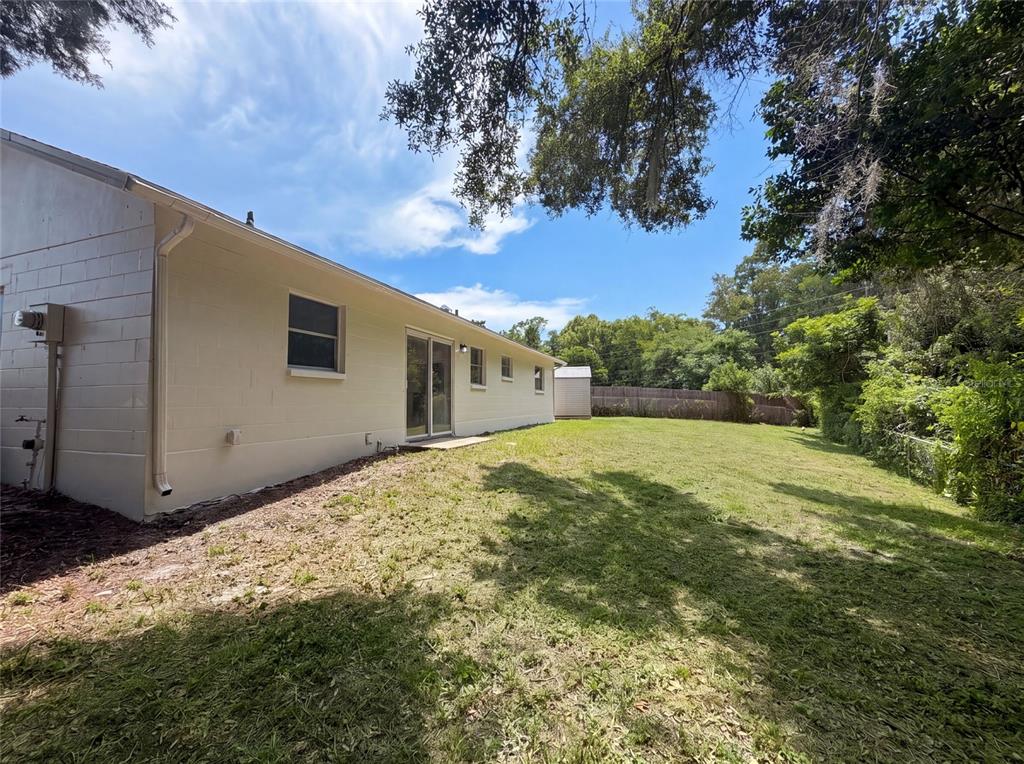The exterior of a light-colored concrete block house features a large backyard and trees — 3730 DEDRICK COURT, NEW PORT RICHEY, FL