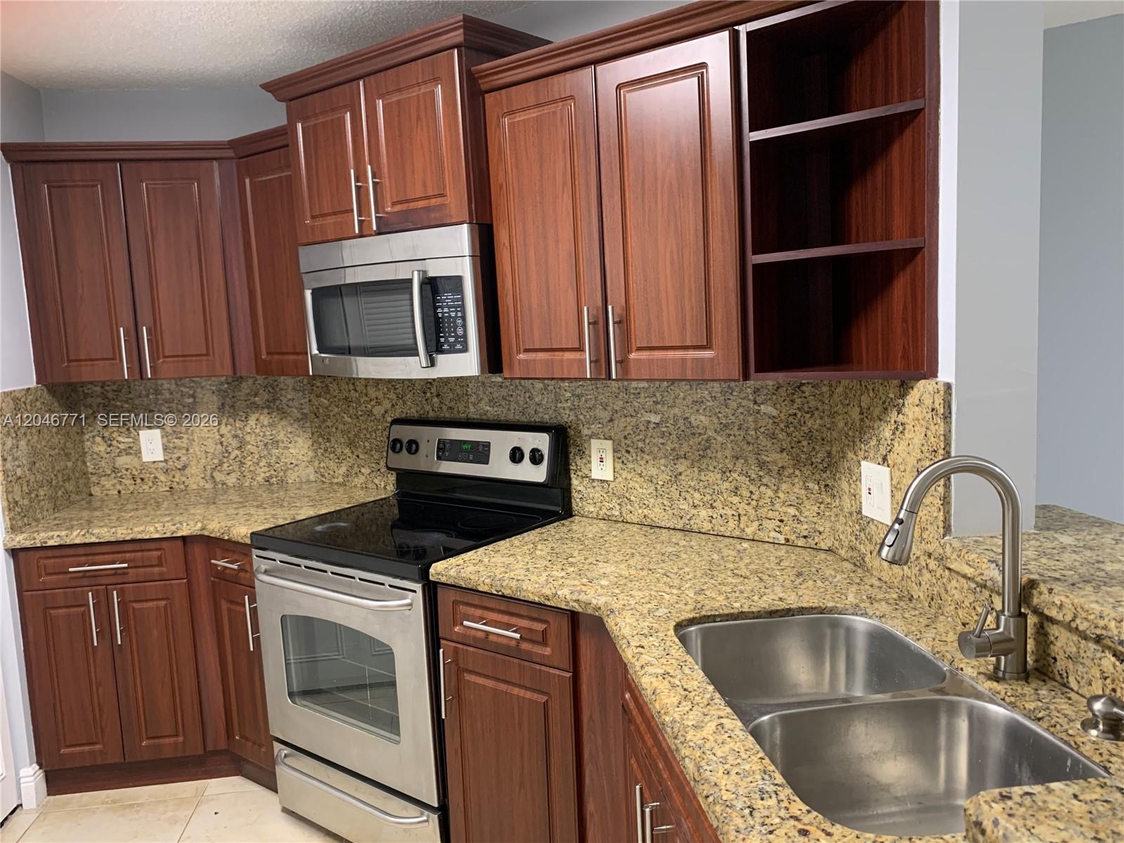 A kitchen features dark wood cabinets, granite countertops, stainless steel appliances, and a double sink — HIALEAH, FL
