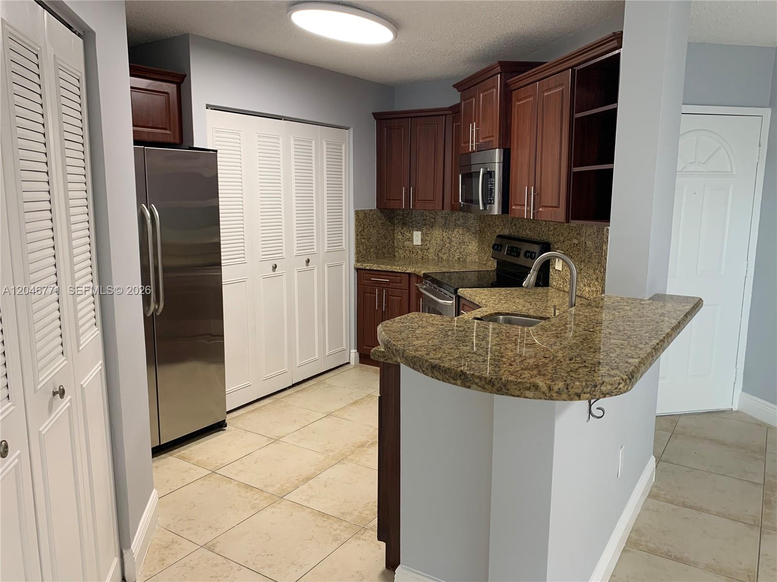 A kitchen features dark wood cabinets, granite countertops, stainless steel appliances, and beige tile flooring — HIALEAH, FL