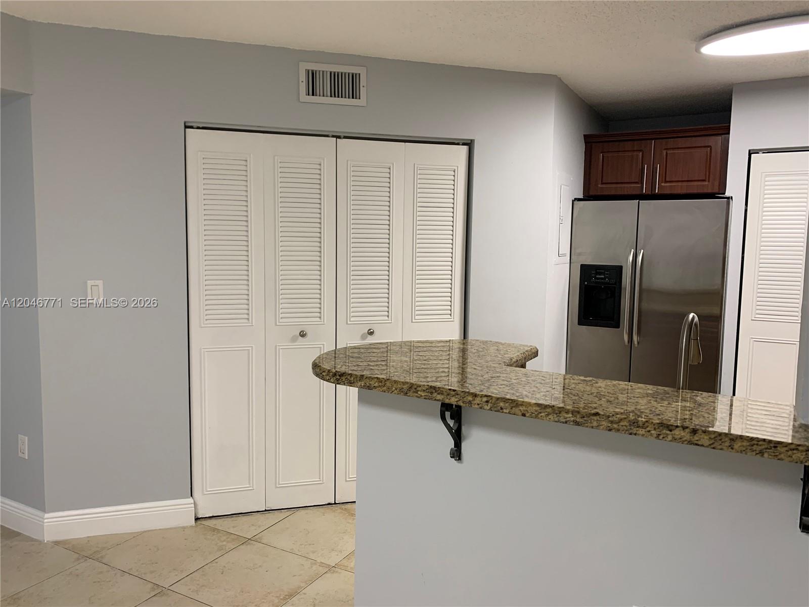 A kitchen features a granite breakfast bar, stainless steel refrigerator, and white louvered closet doors — HIALEAH, FL