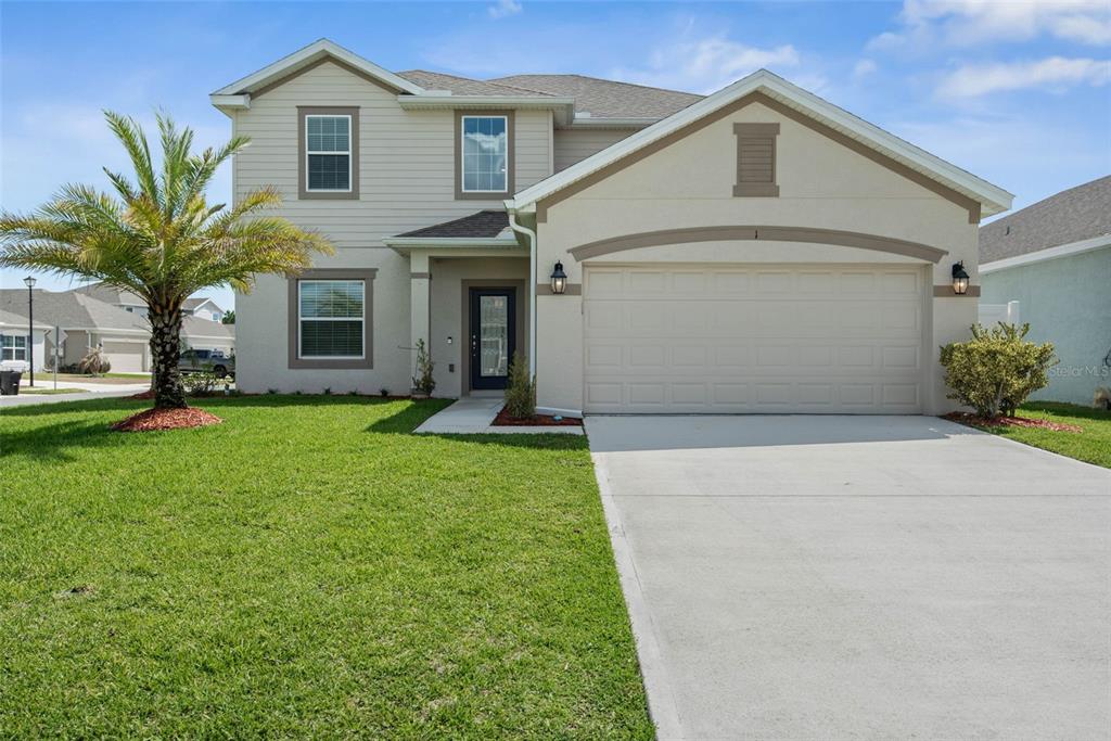 A two-story suburban house with beige siding, a two-car garage, and a front lawn — 1 RIDGE ROAD, PALM COAST, FL