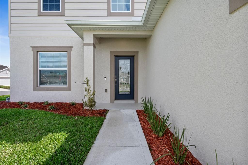 A concrete walkway leads to the front door of a house with beige stucco siding — 1 RIDGE ROAD, PALM COAST, FL