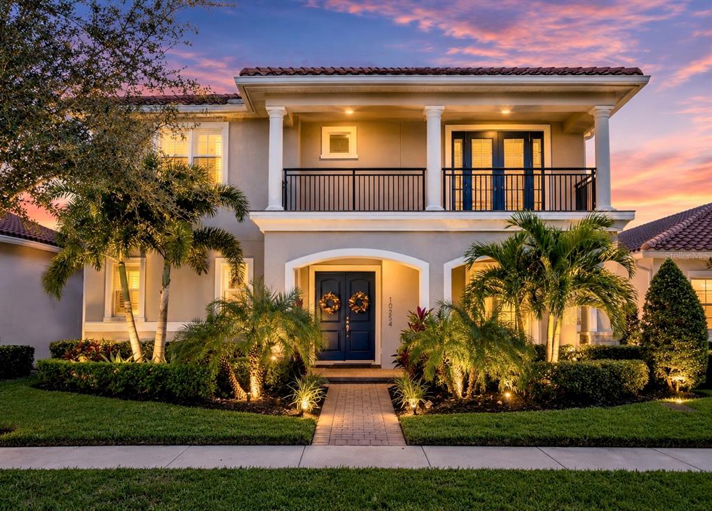 A two-story house with a balcony, arched entryway, and blue double doors at sunset — 10254 BEECHWOOD LANE, ORLANDO, FL