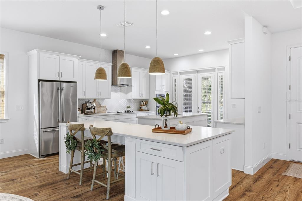 A bright kitchen features white cabinetry, stainless steel appliances, a large island, and wood flooring — 10254 BEECHWOOD LANE, ORLANDO, FL