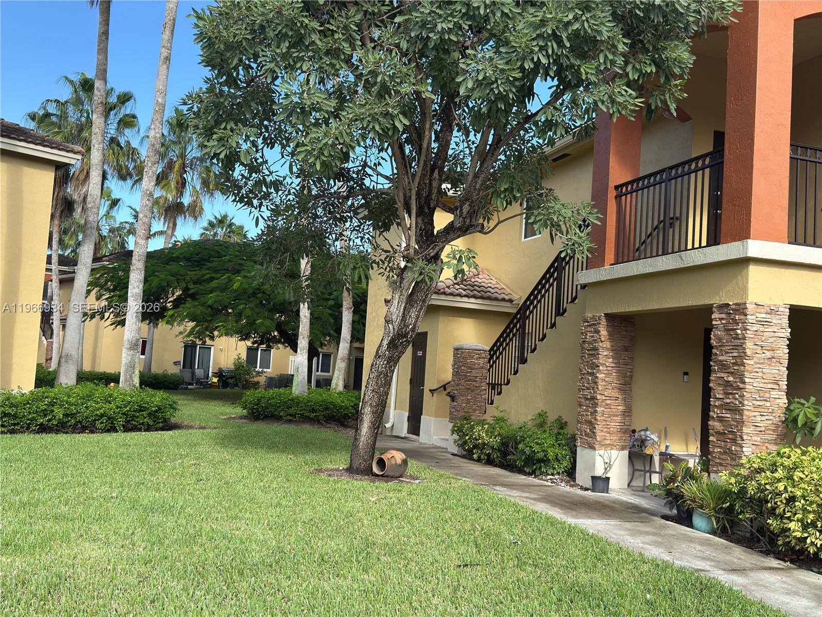 An exterior view of a multi-story apartment building with a staircase and landscaping — 930 NE 34th Ave # 201, Homestead FL 33033, HOMESTEAD, FL