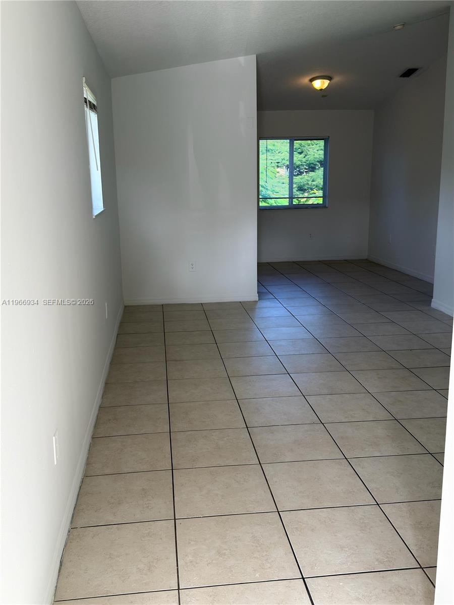 An empty room with light-colored tile flooring and white walls features two windows — 930 NE 34th Ave # 201, Homestead FL 33033, HOMESTEAD, FL