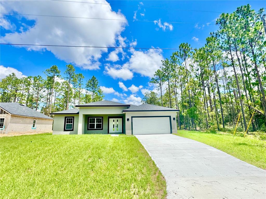 A single-story house with a two-car garage and a concrete driveway sits on a lawn — 1905 W LINDEN DRIVE, CITRUS SPRINGS, FL