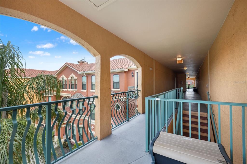 An outdoor apartment corridor features a teal metal railing, concrete flooring, and arched openings — 2738 VIA TIVOLI UNIT 234A, CLEARWATER, FL