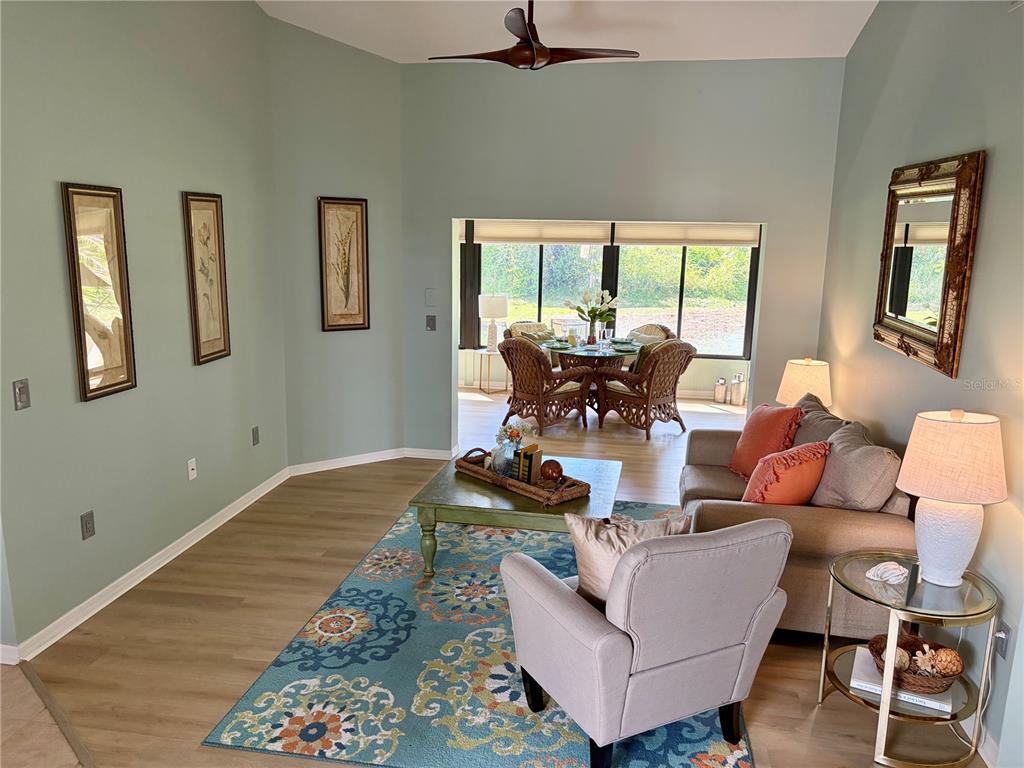 A living room with light green walls, a patterned blue rug, and a dining area beyond — 227 SOUTHAMPTON DRIVE UNIT 289, VENICE, FL