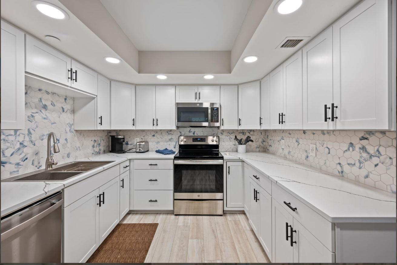 A modern kitchen features white cabinets, stainless steel appliances, quartz countertops, and blue-patterned hexagonal backsplash — 500 Ocean Trail Way # 506, Jupiter FL 33477, JUPITER, FL