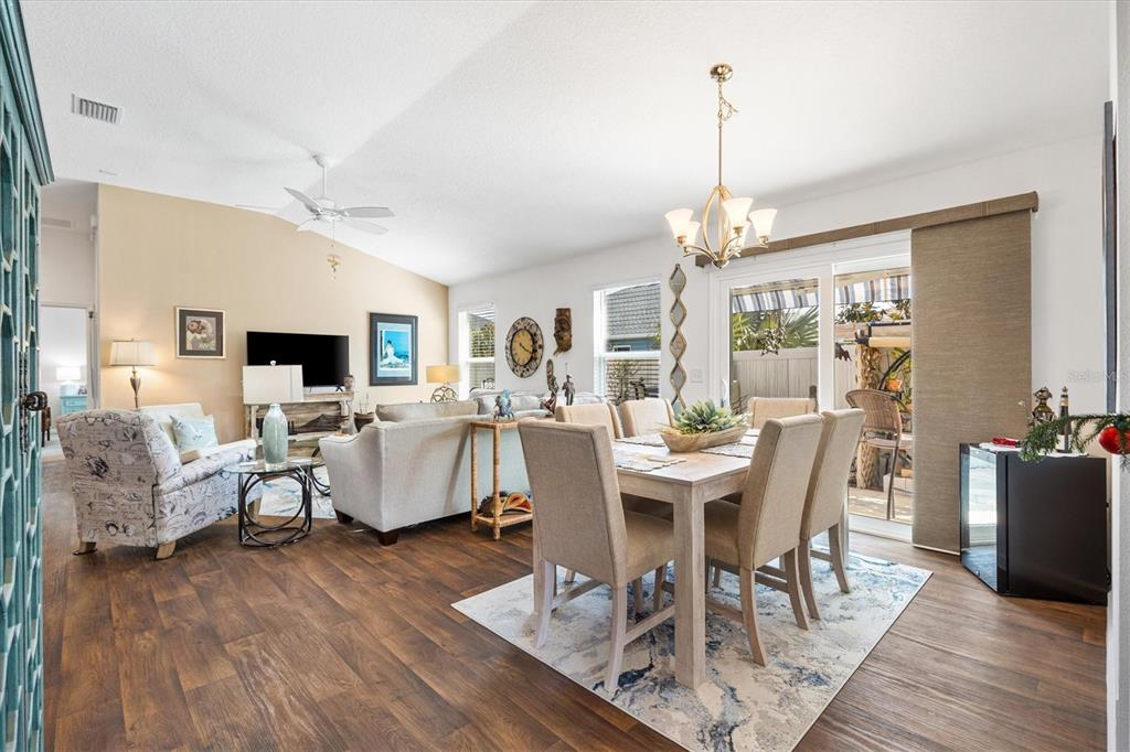 An open-concept living and dining area features wood-look flooring, a vaulted ceiling, and sliding doors — 1773 BLACKWELL LANE, THE VILLAGES, FL