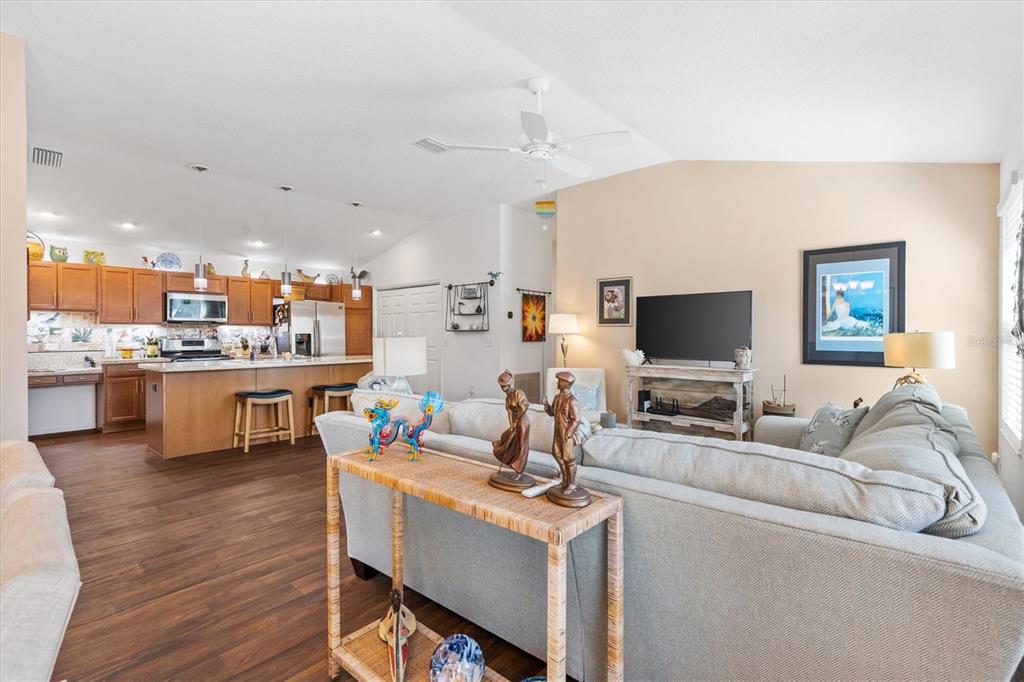 An open-concept living room and kitchen featuring wood flooring, a large sectional, and wooden cabinetry — 1773 BLACKWELL LANE, THE VILLAGES, FL