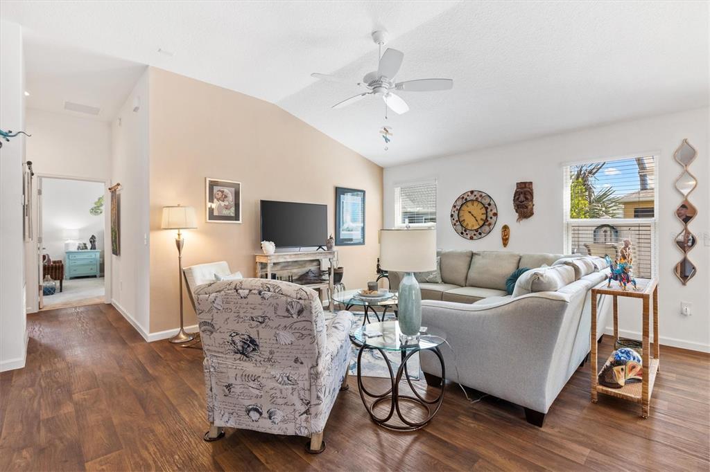A living room features wood-look flooring, a vaulted ceiling, a ceiling fan, and neutral furniture — 1773 BLACKWELL LANE, THE VILLAGES, FL