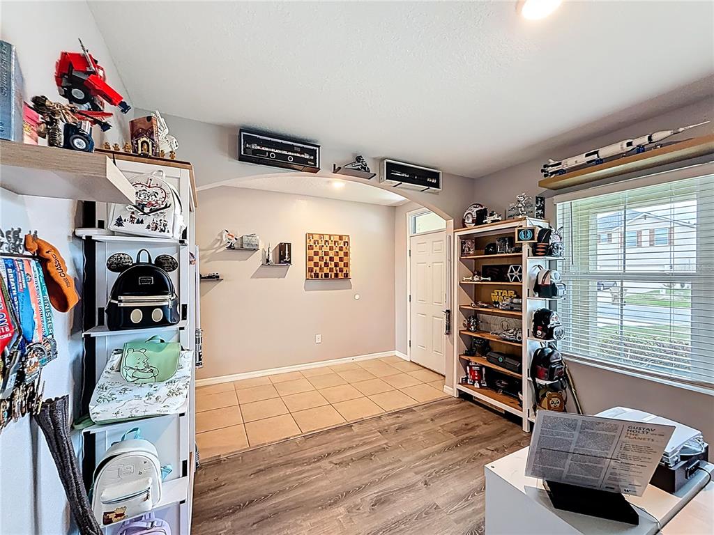 A room with wood-look flooring, tiled entryway, white shelving units, and various collectibles on display — 3689 MAIDENCAIN STREET, CLERMONT, FL