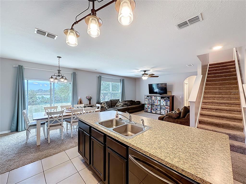 A kitchen island with a double sink overlooks an open-concept living and dining area — 3689 MAIDENCAIN STREET, CLERMONT, FL