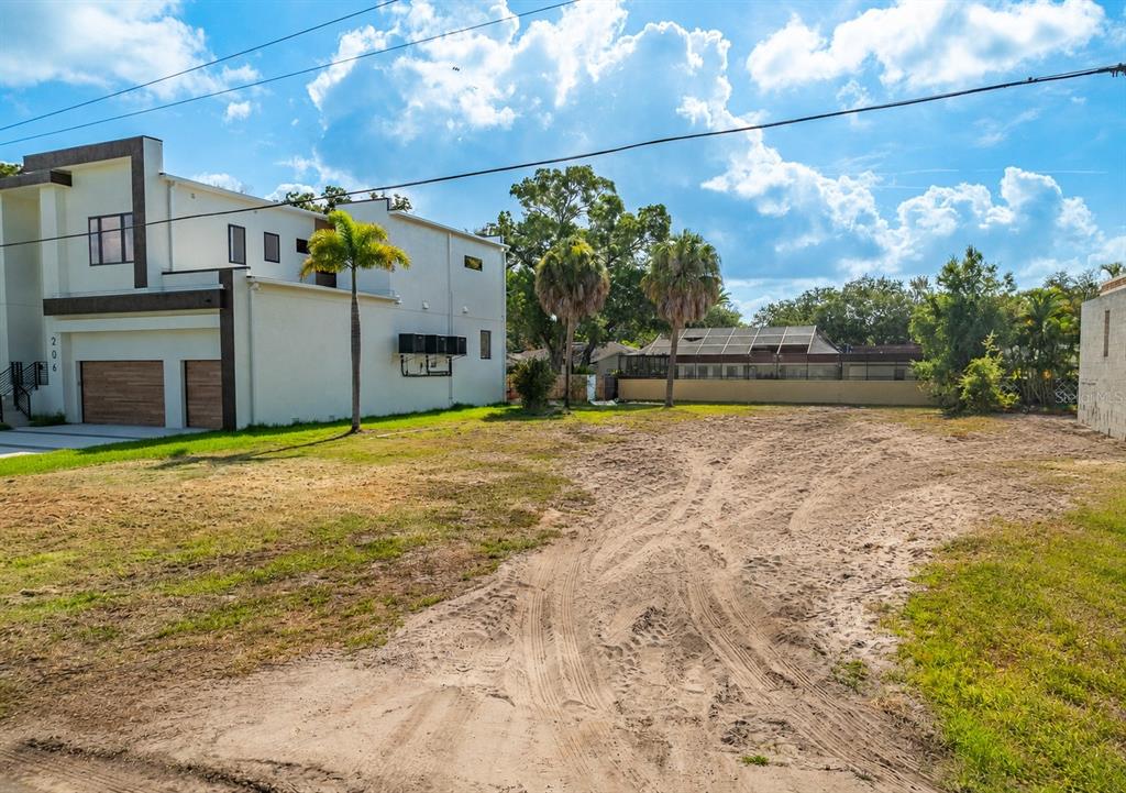 A vacant, sandy residential lot sits next to a modern two-story house with a garage — 208 S TREASURE DRIVE, TAMPA, FL
