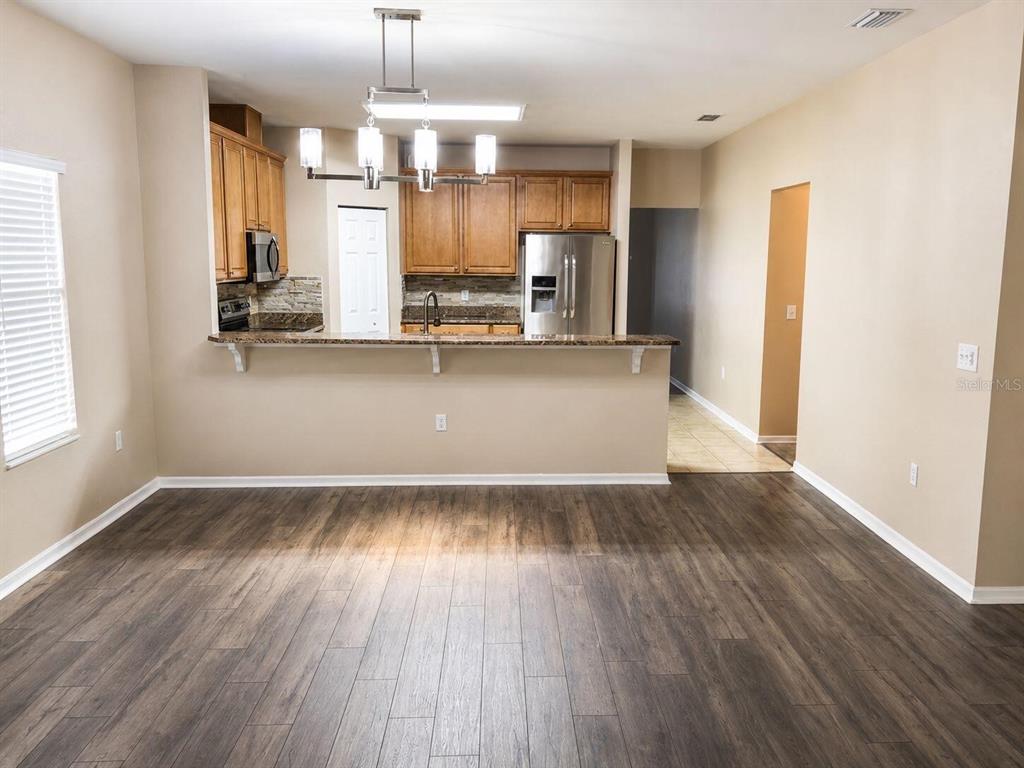 A kitchen with wood cabinets and stainless steel appliances overlooks a dining area with wood-look flooring — 9964 NW 22ND ROAD, GAINESVILLE, FL