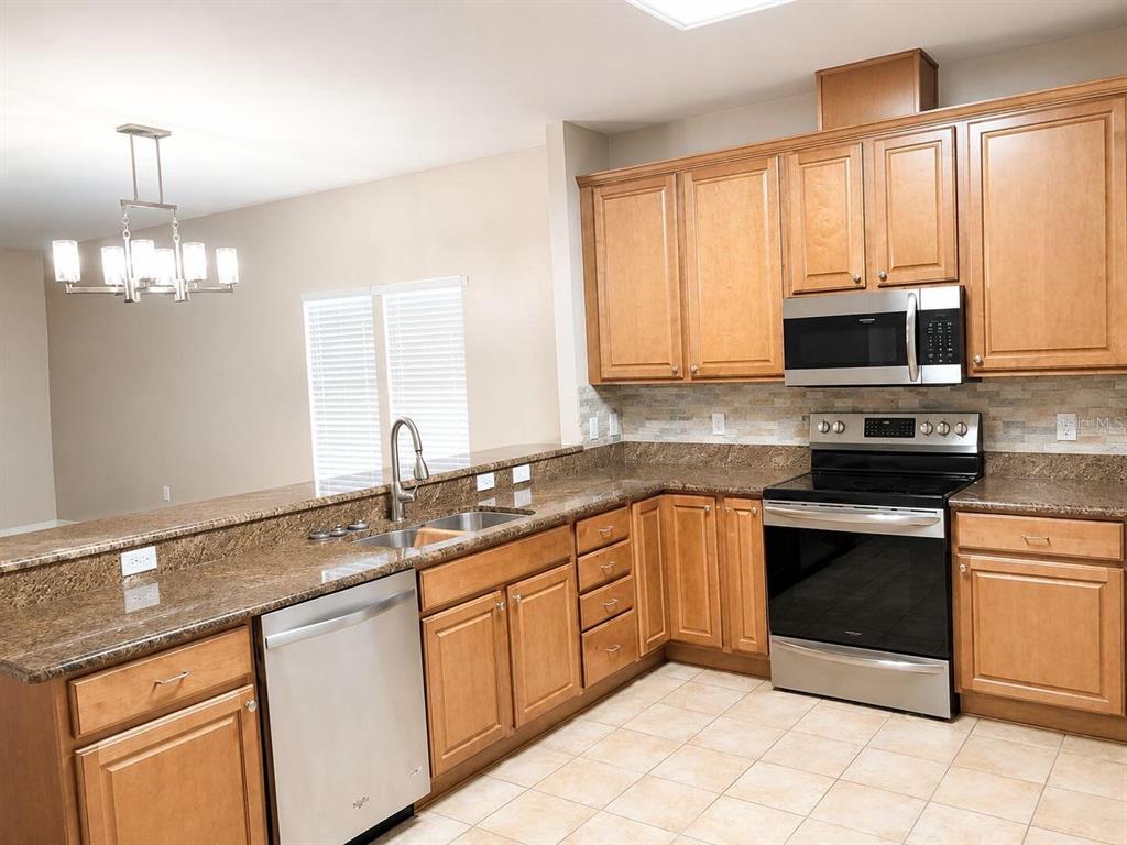 A kitchen features wood cabinets, granite countertops, stainless steel appliances, and tile flooring — 9964 NW 22ND ROAD, GAINESVILLE, FL