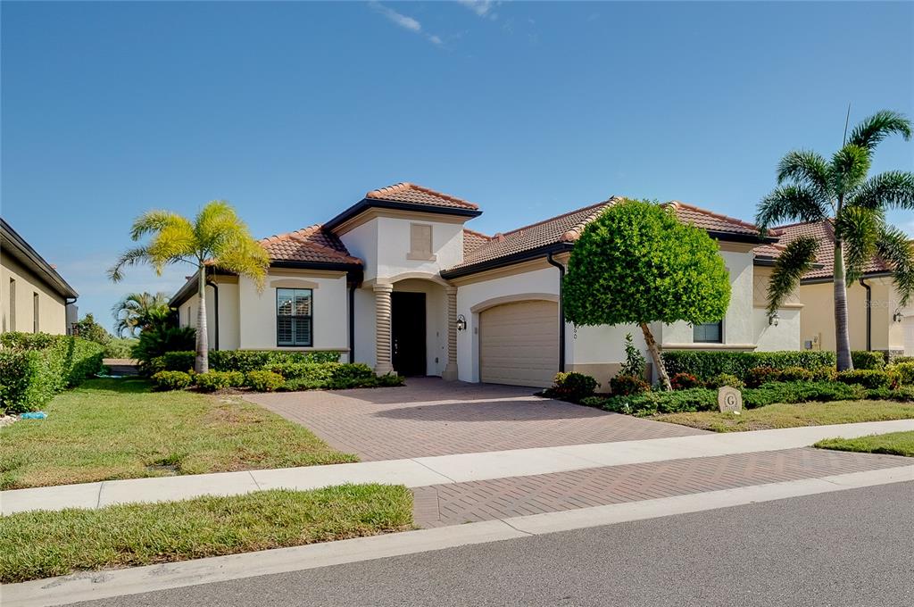 A single-story house with a tiled roof, beige stucco exterior, and a paved driveway — 25060 SPARTINA DRIVE, VENICE, FL