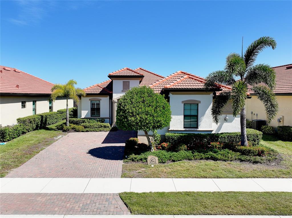 A single-story house with a brick driveway, tile roof, and a palm tree in front — 25060 SPARTINA DRIVE, VENICE, FL