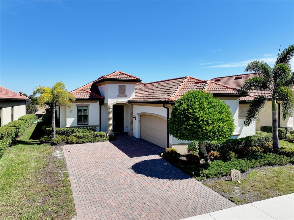 A single-story house with a tiled roof, brick driveway, and palm trees in the front yard — 25060 SPARTINA DRIVE, VENICE, FL