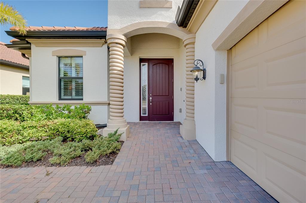 A brick walkway leads to a front entrance with a dark door and two columns — 25060 SPARTINA DRIVE, VENICE, FL