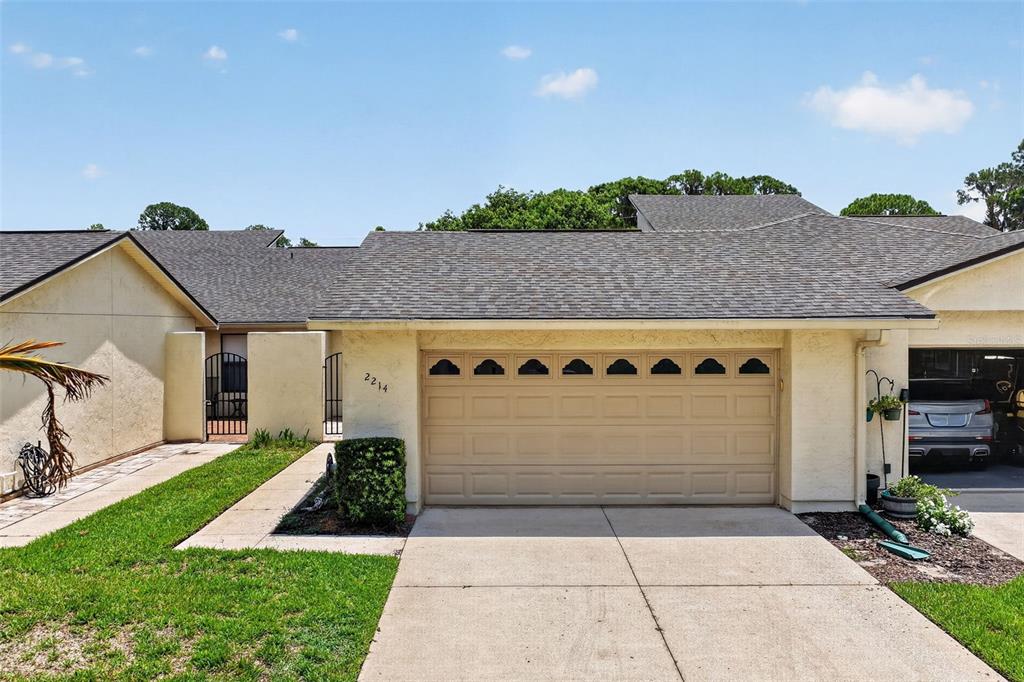A single-story house features a tan garage door, a paved driveway, and a gated entryway — 2214 CYPRESS COVE DRIVE UNIT 4, TAVARES, FL