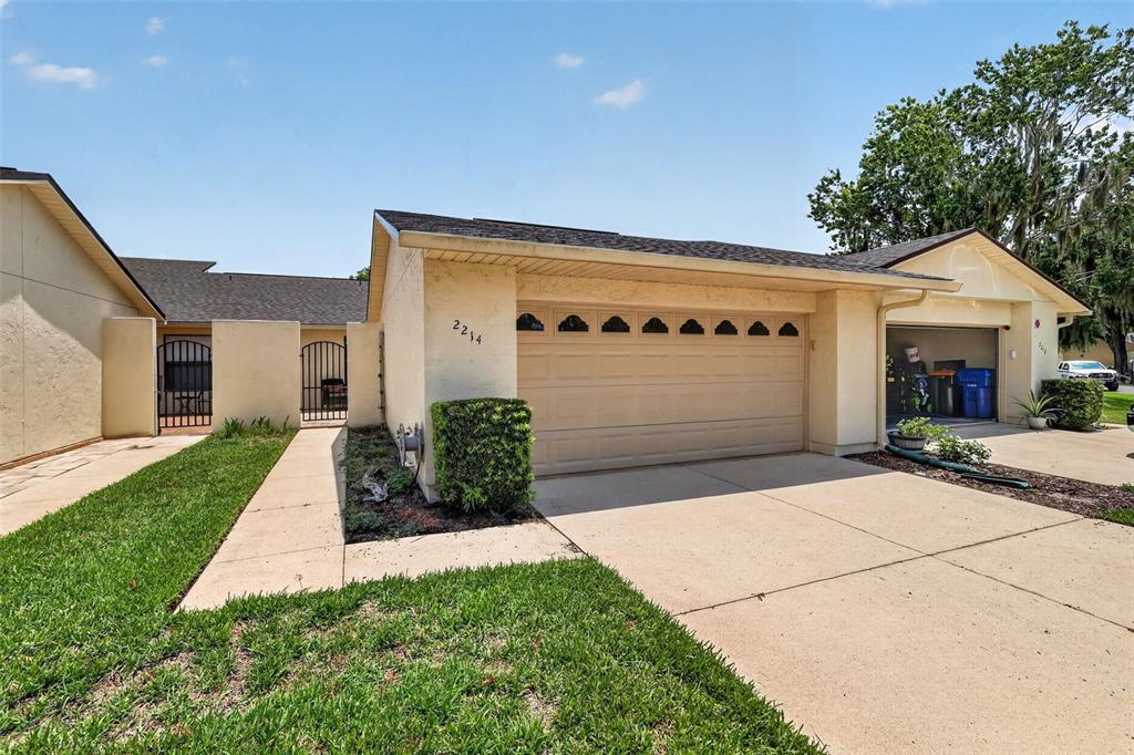 A single-story house exterior features a beige stucco facade, a two-car garage, and gated courtyards — 2214 CYPRESS COVE DRIVE UNIT 4, TAVARES, FL