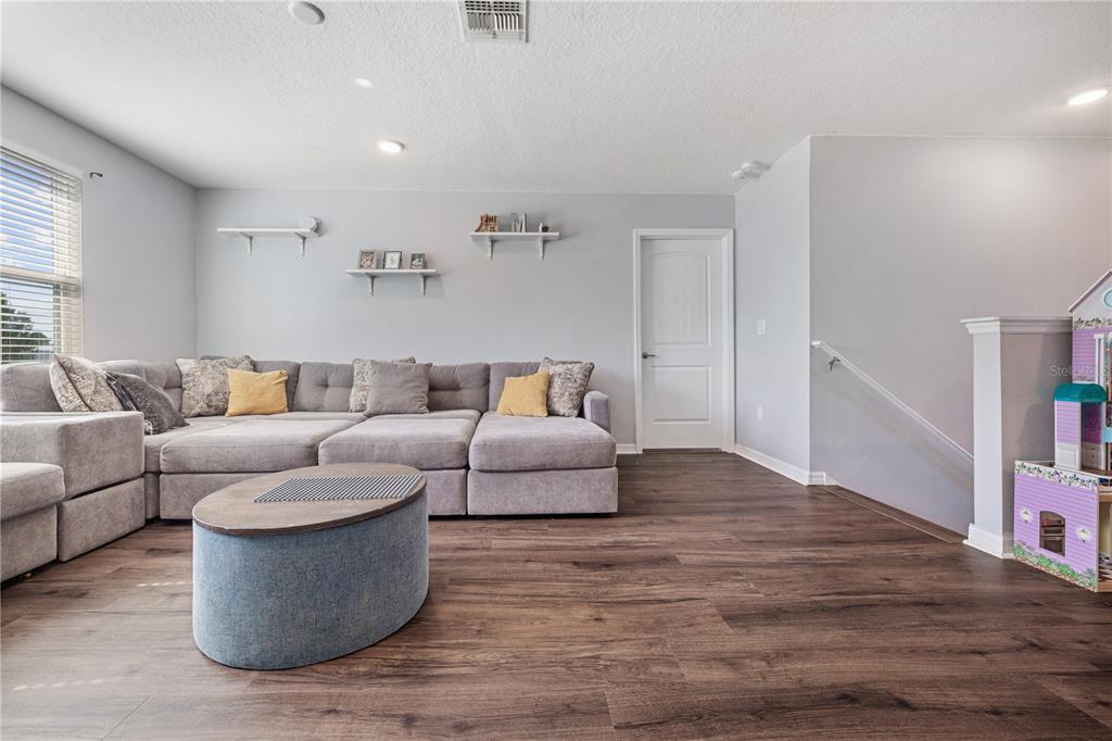 A living room features a large gray sectional sofa, a coffee table, and wood-look flooring — 16720 MOONER PLANK CIRCLE, WIMAUMA, FL