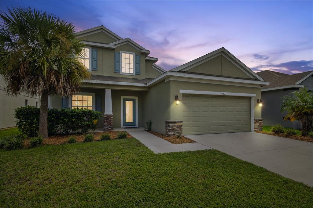 A two-story suburban house with a green exterior, a two-car garage, and a palm tree — 16720 MOONER PLANK CIRCLE, WIMAUMA, FL
