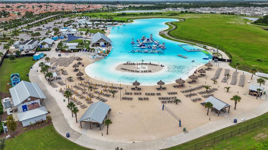 An aerial view shows a large swimming lagoon with an inflatable obstacle course and beach — 16720 MOONER PLANK CIRCLE, WIMAUMA, FL