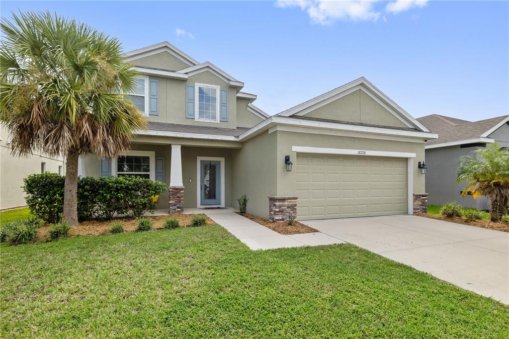 A two-story house with a light green stucco exterior, a two-car garage, and a palm tree — 16720 MOONER PLANK CIRCLE, WIMAUMA, FL
