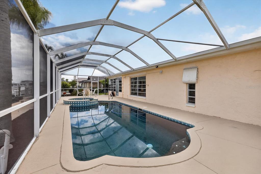 A screened-in patio features a swimming pool with an attached spa and beige concrete decking — 5110 PORPOISE PLACE, NEW PORT RICHEY, FL