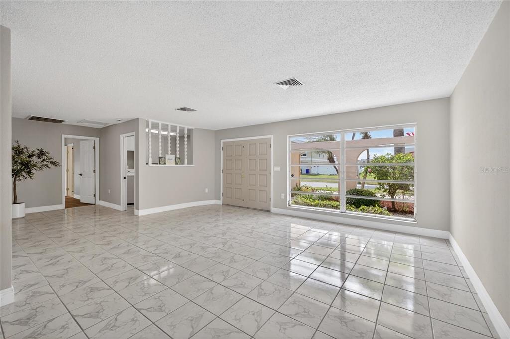 An empty living room features white marble-look tile flooring, light gray walls, and a large window — 5110 PORPOISE PLACE, NEW PORT RICHEY, FL