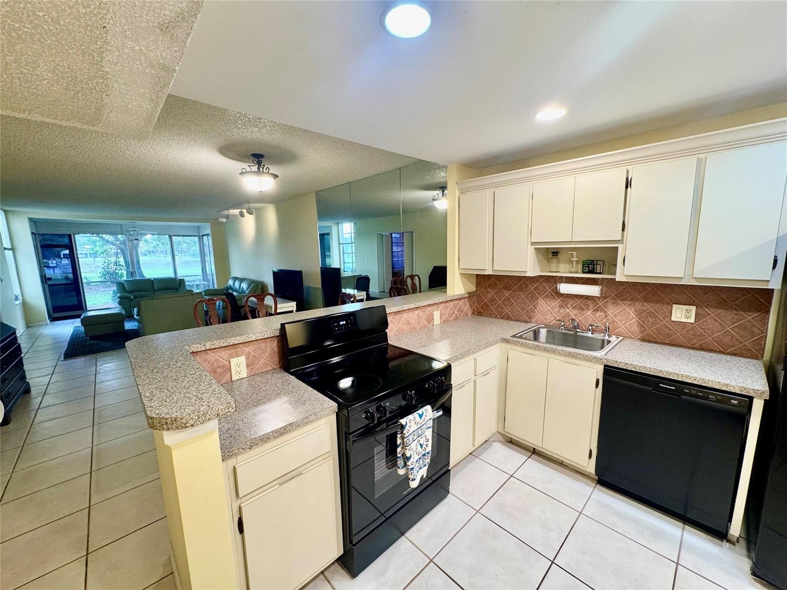 A kitchen with white cabinets, black appliances, and granite countertops overlooks a living area — 804 Cypress Boulevard # 106, Pompano Beach FL 33069, POMPANO BEACH, FL