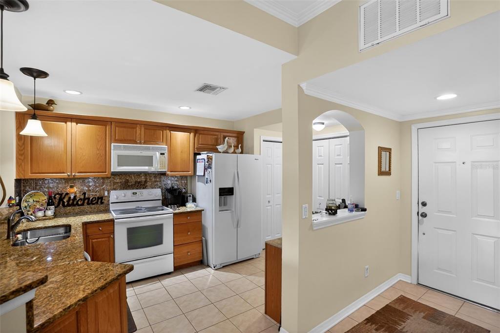 A kitchen with wood cabinets, granite countertops, and white appliances opens to an entryway — 4263 LIRON AVENUE UNIT 101, FORT MYERS, FL