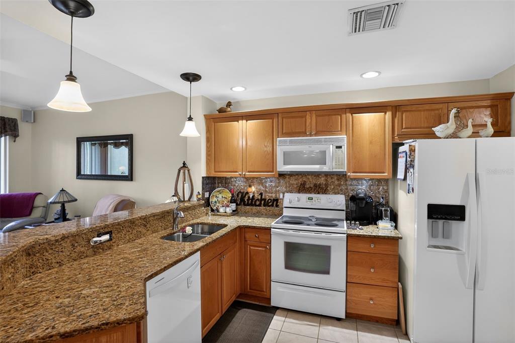 A kitchen features wood cabinets, granite countertops, white appliances, and a breakfast bar — 4263 LIRON AVENUE UNIT 101, FORT MYERS, FL