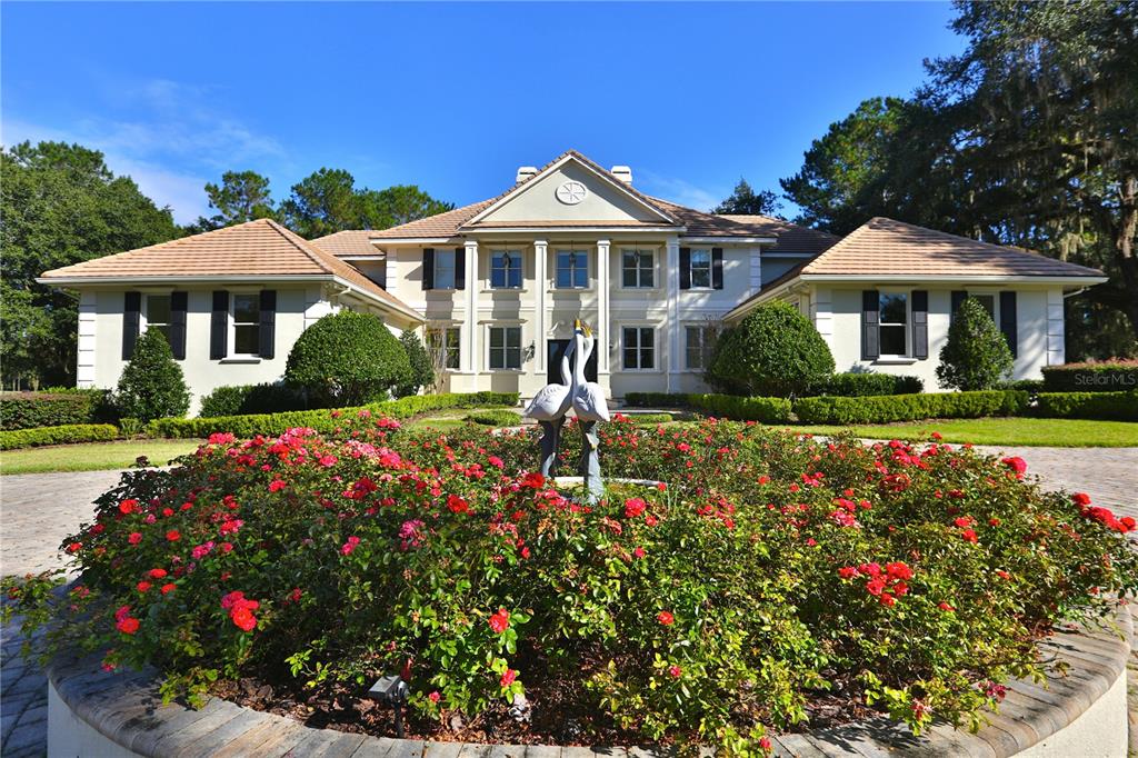 A large two-story house with a circular rose garden and flamingo statue in the foreground — 4026 NW 85TH TERRACE, OCALA, FL